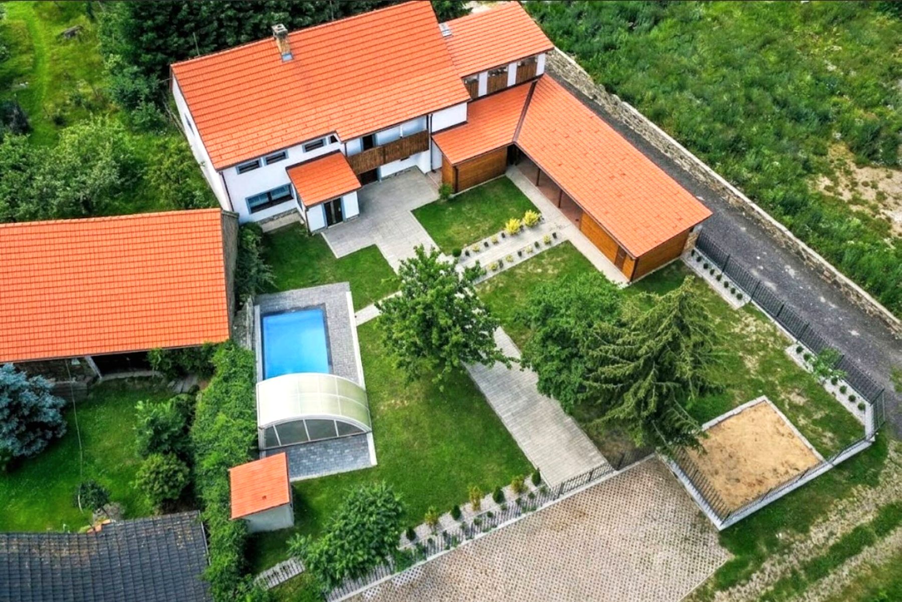 Letecký pohled na areál: chata s oranžovou střechou, dvůr s bazénem, zahrada a přístřešky