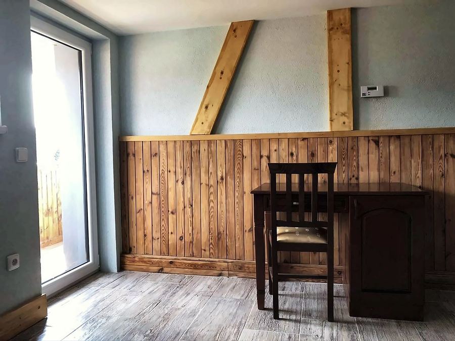 Pokoj s dřevěným obložením, psacím stolem a oknem na balkon