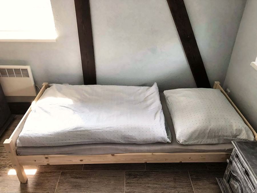 Dřevěná postel s bílým povlečením pod šikmým trámem