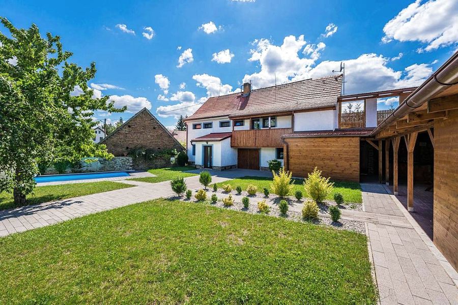 Zahrada s trávníkem a záhony, vlevo bazén, vzadu chata a dřevěné přístřešky